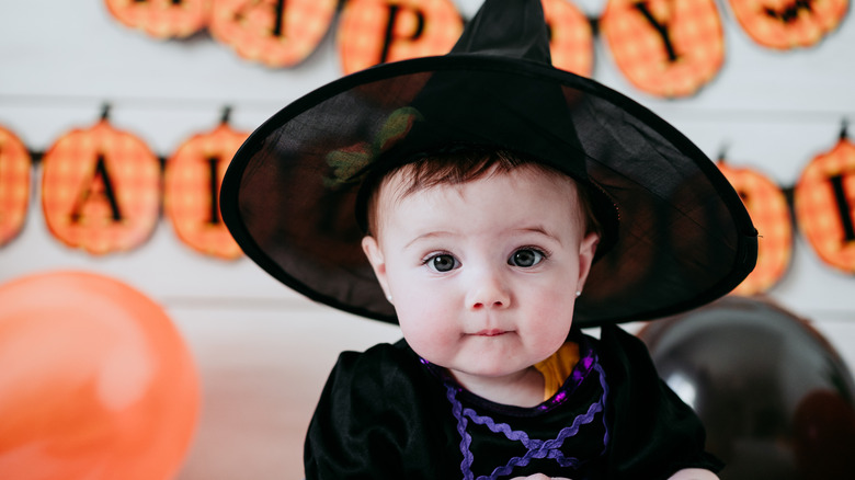Baby girl in witch hat with pumpkins behind her