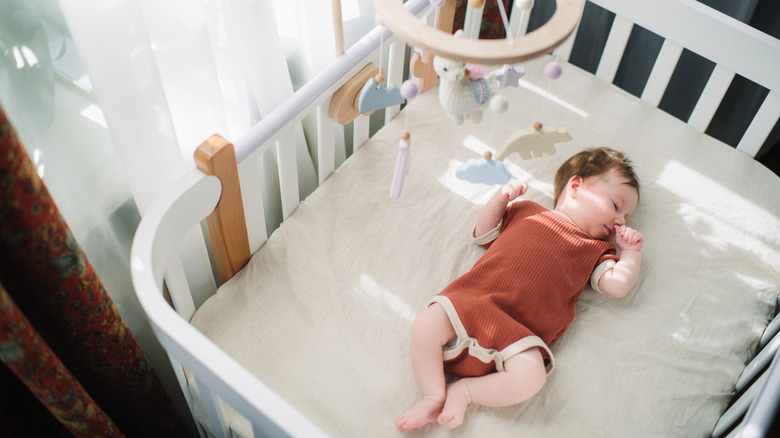 A baby sleeps in a crib with a mobile overhead