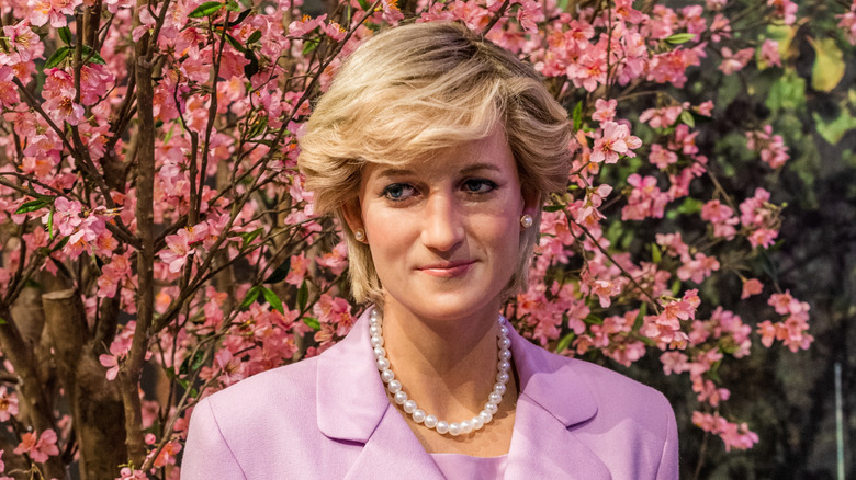 Princess Diana standing in front of a blooming pink tree wearing a purple suit and a pearl necklace