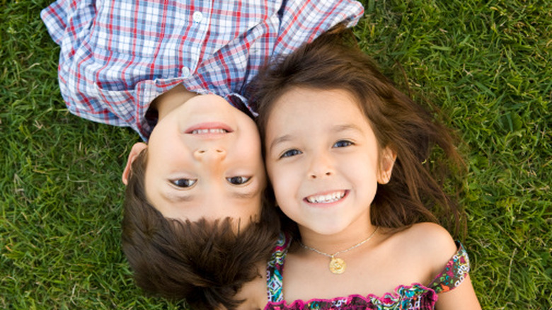 Boy and girl lying on the grass looking into camera