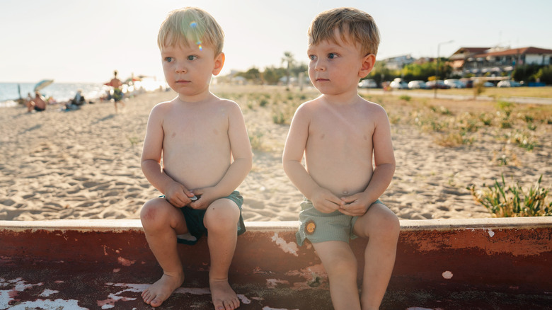 Blond and brunette twins sitting on curb at the beach