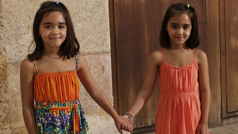Brunette sisters in orange sundresses holding hands