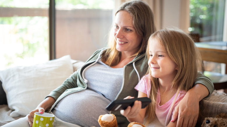 Pregnant mom with daughter sitting on the couch watching TV