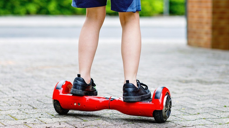 A child in black sneakers and blue shorts, balancing on a red hoverboard