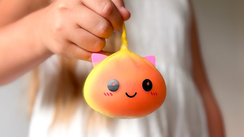 A girl in a white dress holding a yellow, orange, and pink squishy cat toy