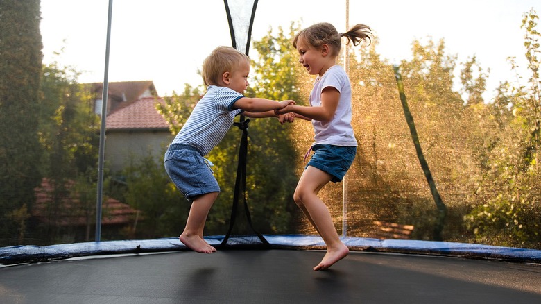 Two small kids holding hands while jumping on a large outdoor trampoline