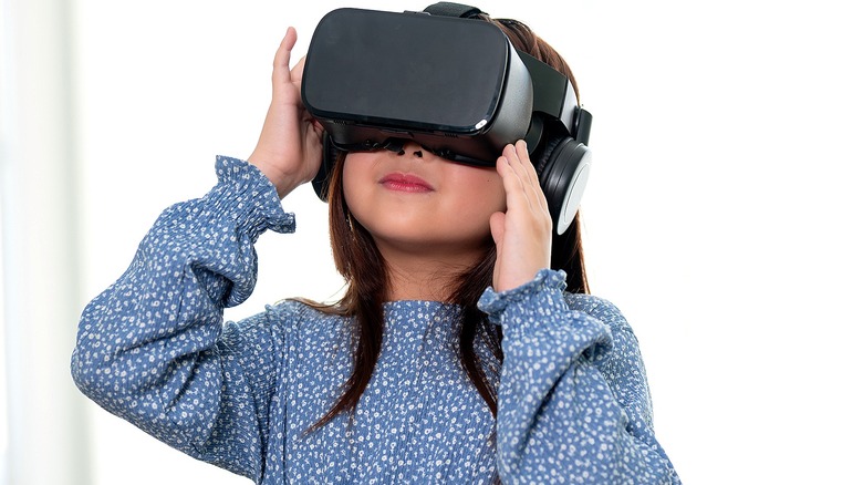 Young girl in a blue dress with white flowers wearing a black VR headset
