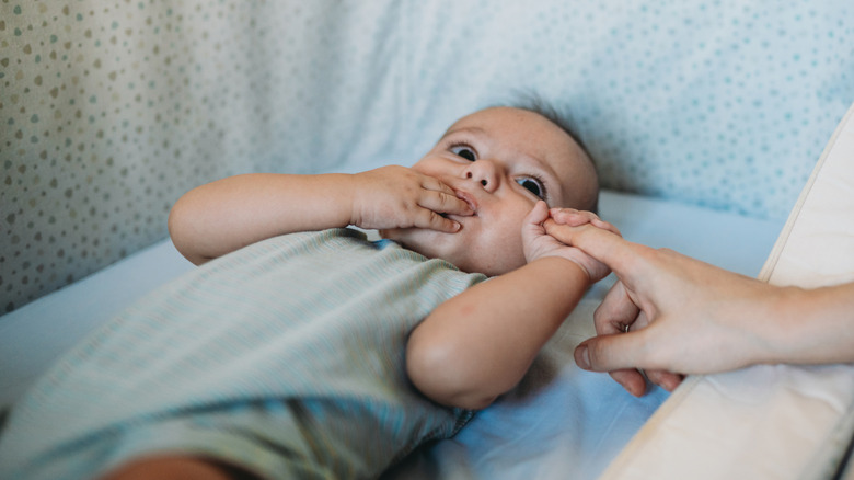Baby in a bassinet next to a bed holding finger