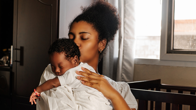 Woman holding newborn in front of crib