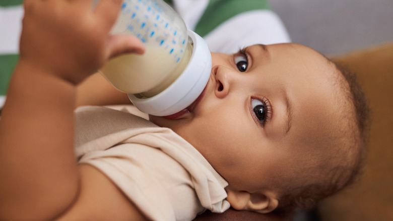 baby drinking and holding bottle and looking out to the side
