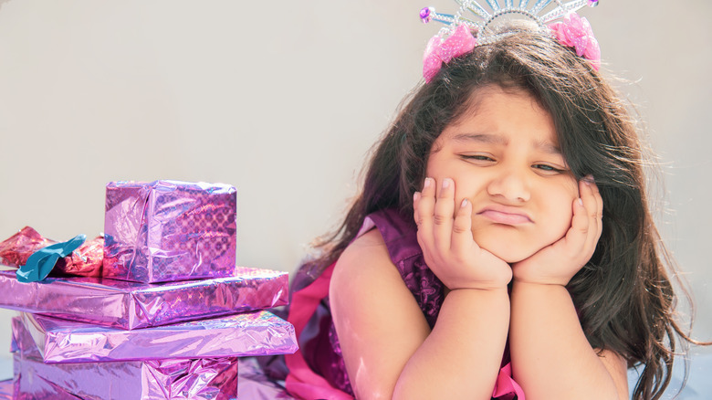 A birthday girl sits with her chin in her hands unimpressed by the pile of birthday presents beside her