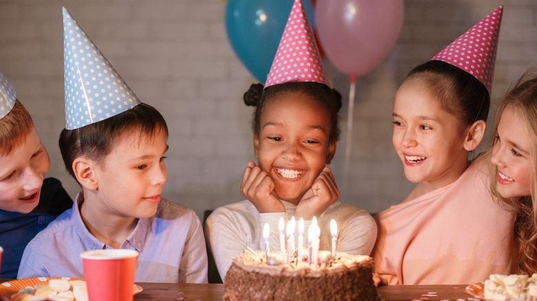 A birthday girl gets ready to blow out the candles on her cake, surrounded by friends