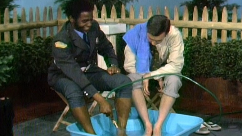 Officer Clemmons and Mister Rogers dip their feet in a wading pool together