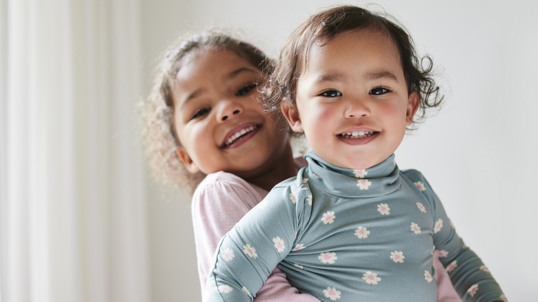 An older sibling child hugs a younger sibling child