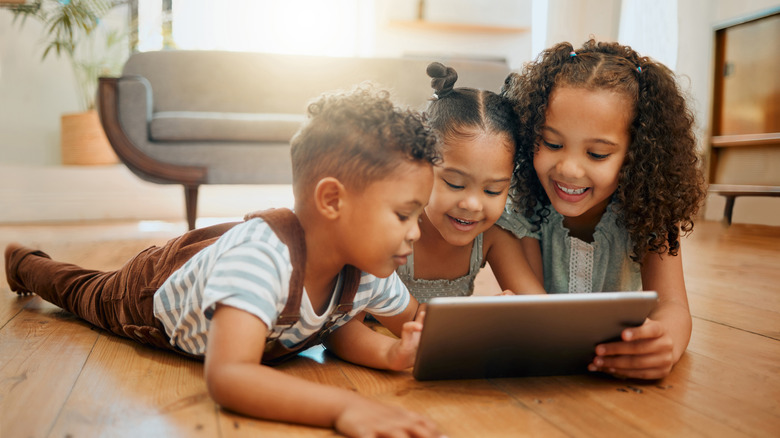 Three young children sit in front of an iPad sprawled out on the floor