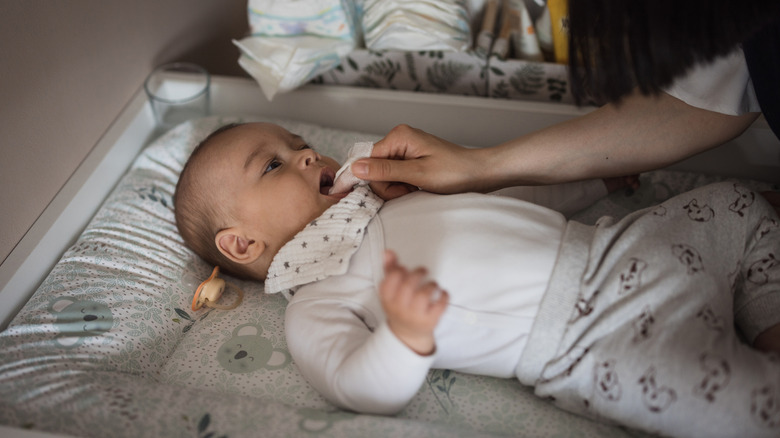 Adult hand with a gloved finger reaching in to a baby's mouth to perform a gum cleaning at home.
