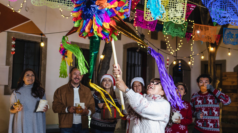 woman hitting a pinata outside with friends surrounding her and watching