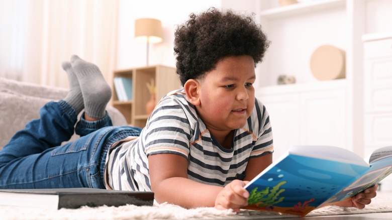 Boy in striped shirt lying on his stomach reading