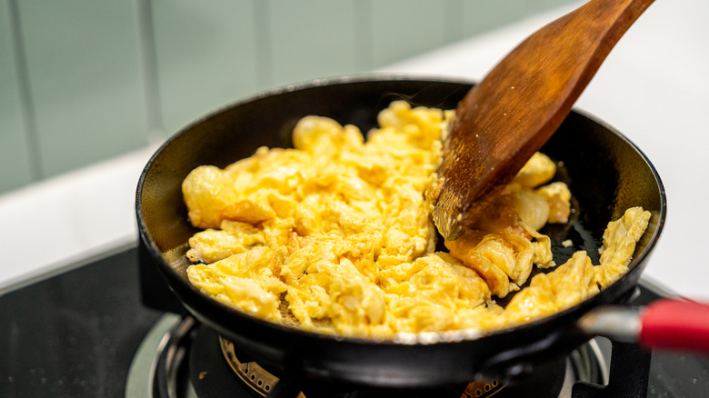 Scrambled eggs being prepared in a pan using a wooden spatula