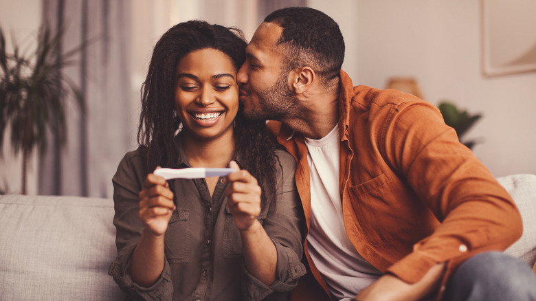 A man kisses a woman on the cheek as she looks at a pregnancy test
