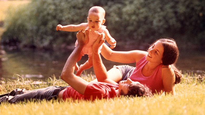 1970s era mom and dad holding up baby in a field