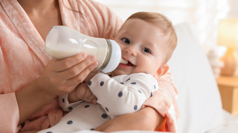 Six month old baby smiling while taking a bottle
