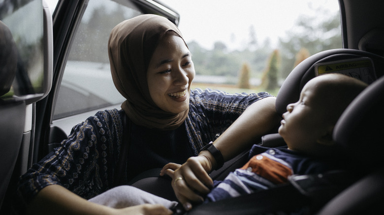 A mother secures a baby in an infant carseat in the back seat of a car