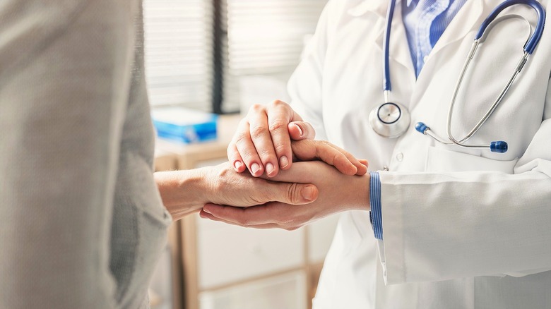 A doctor in a white lab coat holding a patient's left hand with both hands