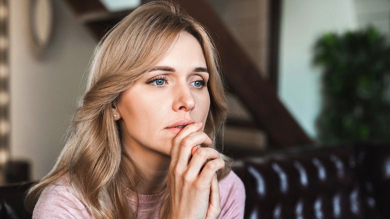 A woman with dirty blonde hair looking thoughtful with her hands clasped together at her mouth