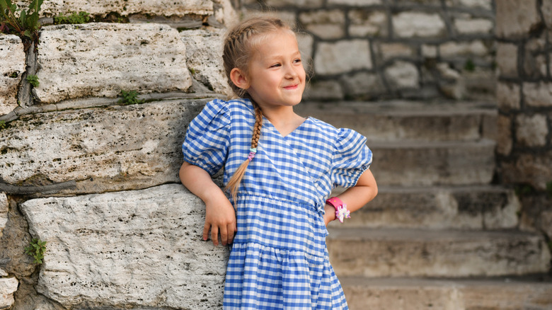 young girl standing in front of a castle wearing blue and white checkered dress