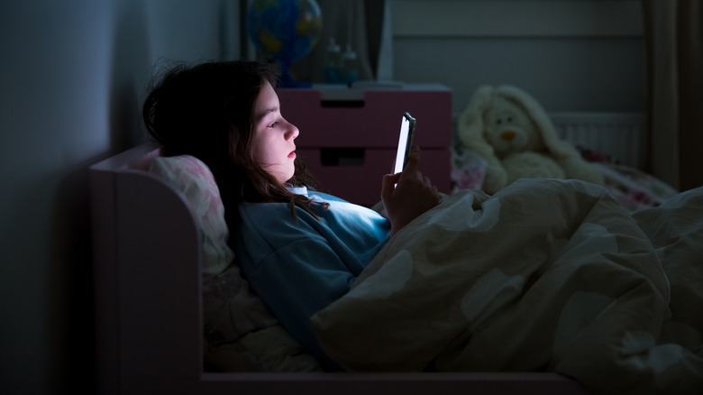 Child using phone in bed at night