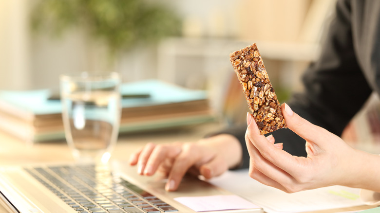 woman holding a protein bar at her desk