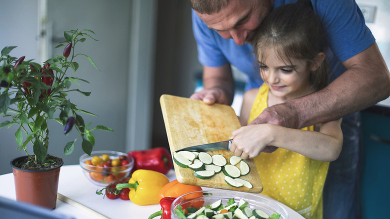 Father helps daughter put cucumbers in a salad