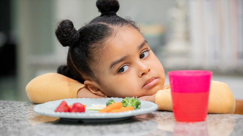 A young girl is not happy with her plate of vegetables