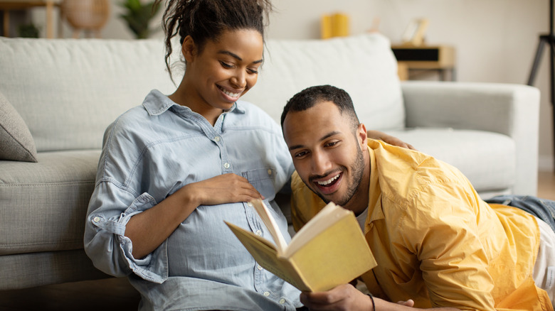 pregnant woman and man look at book together while relaxing on sofa