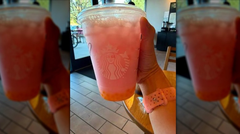Hand holding pink and orange Starbucks drink