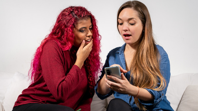 Two seated women appearing shocked at something on a cell phone