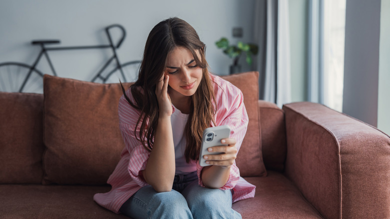 Woman sitting on sofa looking at phone and frowning