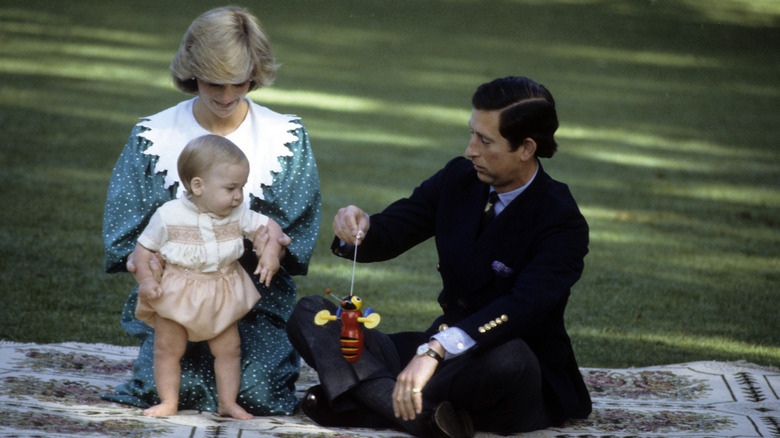 Princess Diana holding William, Prince of Wales while King Charles holds a toy