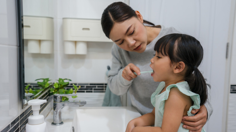 mom helping child brush teeth