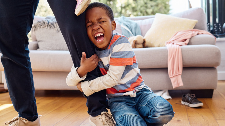 A boy site on the floor hugging the leg of an adult with an emotional expression on his face