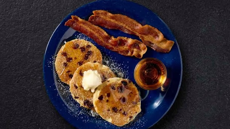 Cracker Barrel mini chocolate chip pancakes with two strips of bacon and a cup of syrup