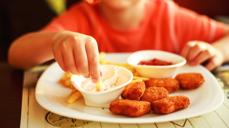 A child dips a fry into sauce on a plate with chicken nuggets