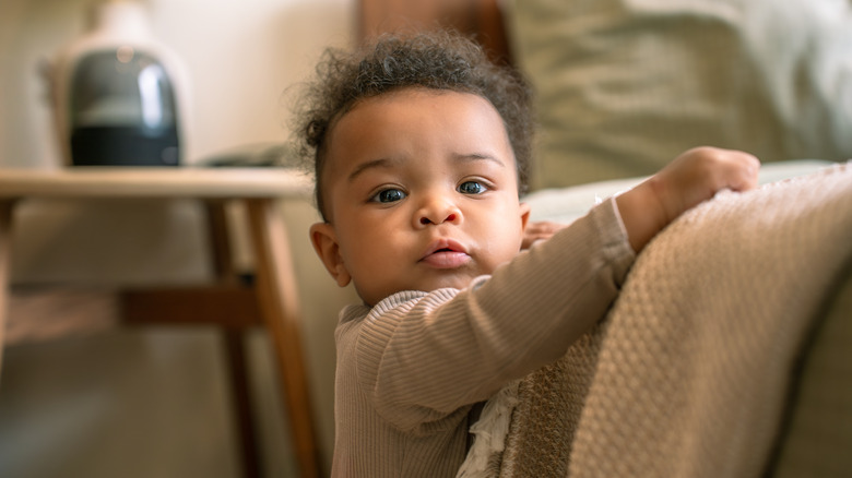 A baby pulling up on a bed and looking at the camera