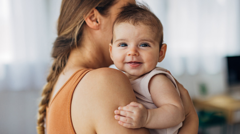 A mother holds her baby girl over her shoulder, the baby looks at the camera