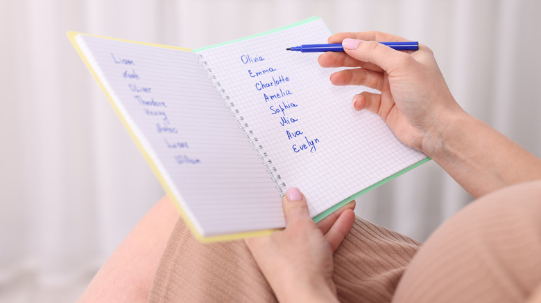 A pregnant person holds a notebook with potential baby names listed