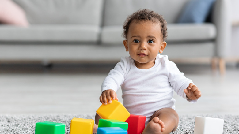 A baby boy sits on the floor playing with blocks