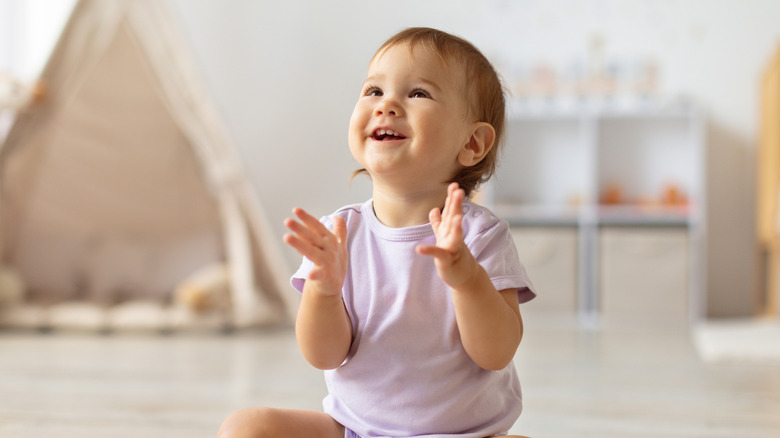A baby girl claps and smiles looking up