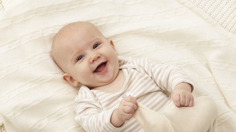 A baby lies on the bed smiling