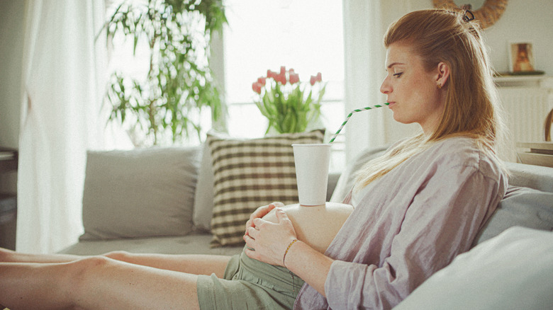 pregnant young mother drinking beverage from a straw while cup sits on her bump